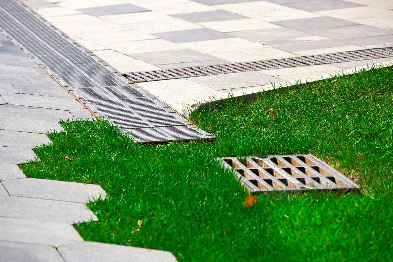 Pavement with stone tiles decorative pattern and trimmed green lawn on summer park with drain system